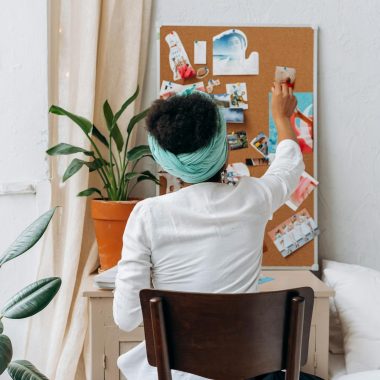 A woman in a cozy room organizing a vision board with photos and ideas.